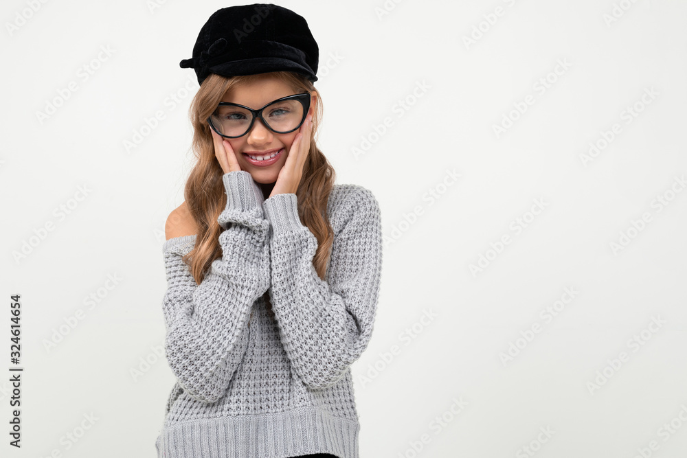 Pretty little girl in grey blouse, cap and glasses smiles isolated on white background Pretty little girl in grey blouse, cap and glasses smiles isolated on white background