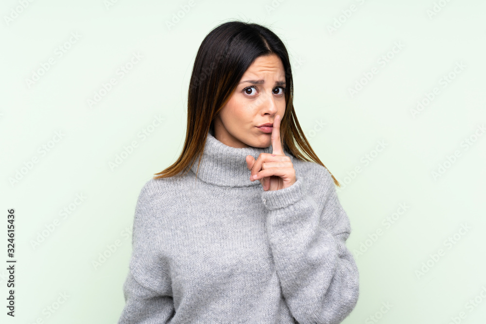 Woman wearing a sweater over isolated green background doing silence gesture Woman wearing a sweater over isolated green background doing silence gesture
