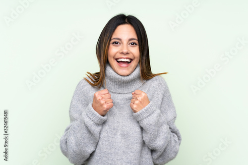 Woman wearing a sweater over isolated green background celebrating a victory