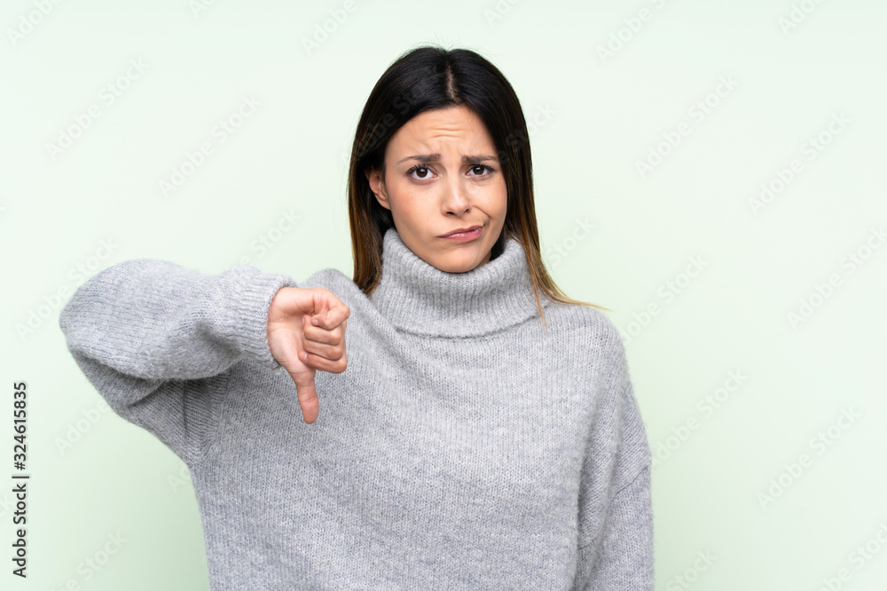 Woman wearing a sweater over isolated green background showing thumb down sign Woman wearing a sweater over isolated green background showing thumb down sign