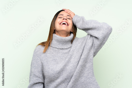 Woman wearing a sweater over isolated green background laughing