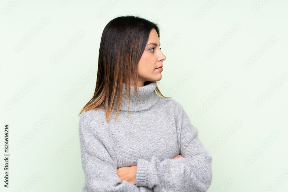 Woman wearing a sweater over isolated green background looking side Woman wearing a sweater over isolated green background looking side