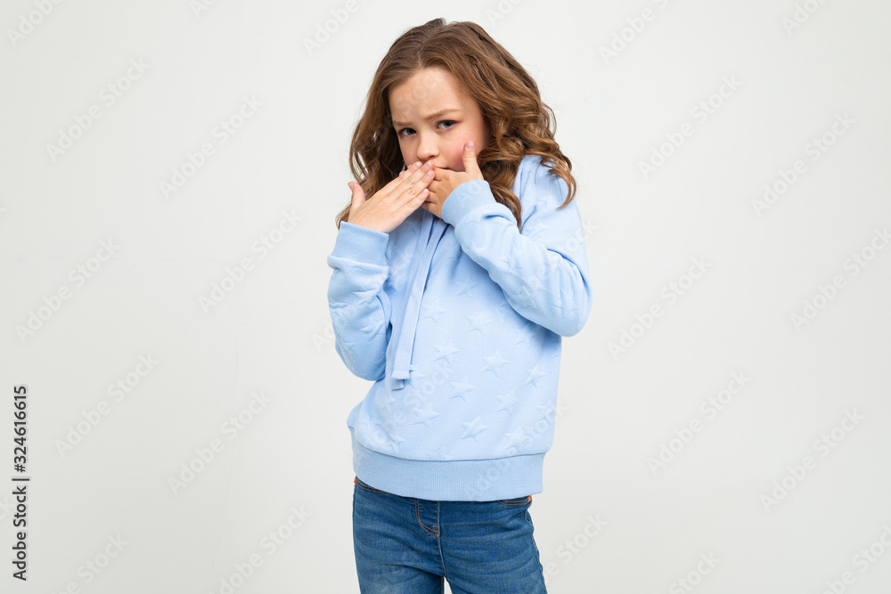 European teenage girl in a blue hoodie covered her mouth on a white background with copy space European teenage girl in a blue hoodie covered her mouth on a white background with copy space