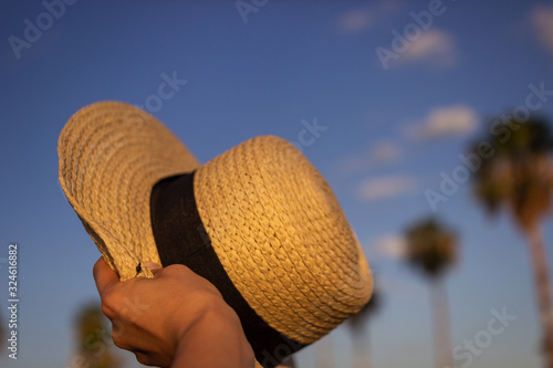 Straw hat close-up on a background of sky and palm trees. Summer background for greeting cards with hat in hand. Relaxation