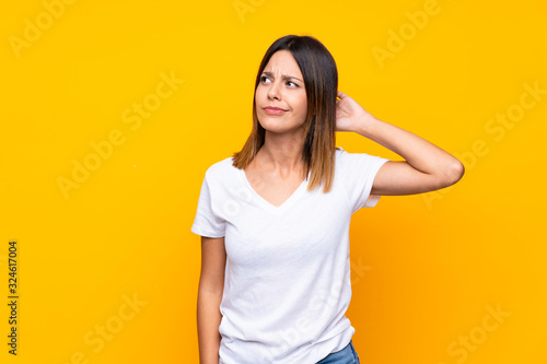 Young woman over isolated yellow background having doubts