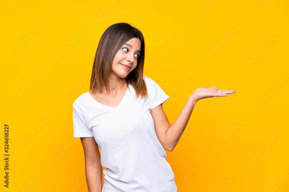 Young woman over isolated yellow background holding copyspace with doubts Young woman over isolated yellow background holding copyspace with doubts