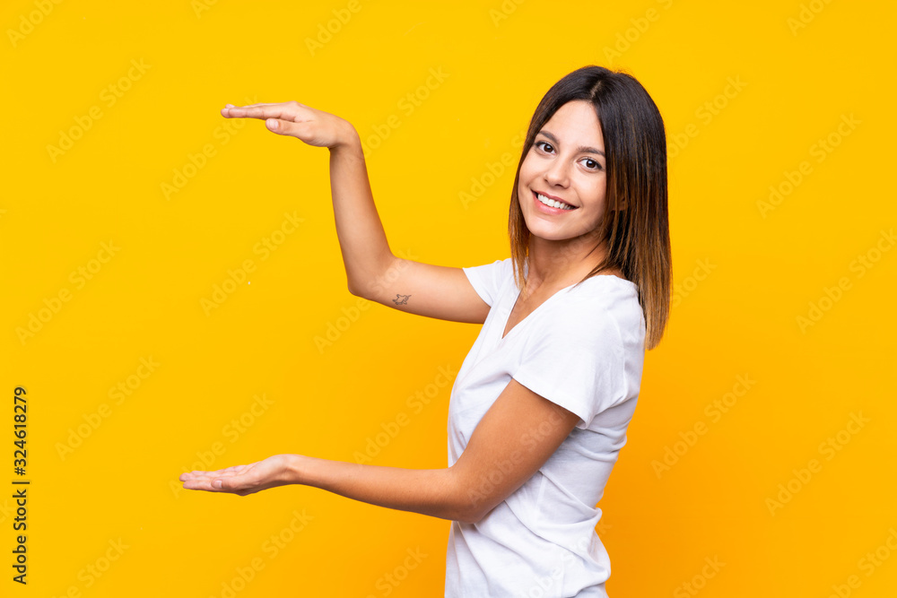 Young woman over isolated yellow background holding copyspace to insert an ad Young woman over isolated yellow background holding copyspace to insert an ad