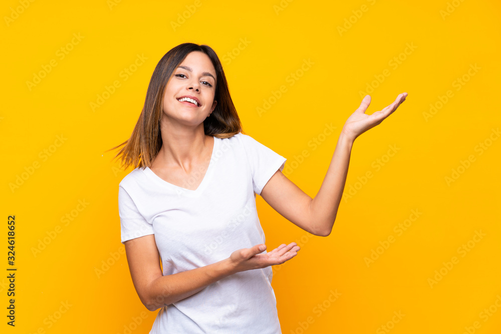 Young woman over isolated yellow background extending hands to the side for inviting to come Young woman over isolated yellow background extending hands to the side for inviting to come