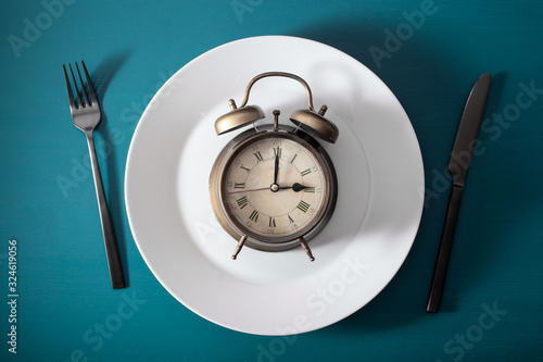 concept of intermittent fasting, ketogenic diet, weight loss. fork and knife on a plate and alarmclock