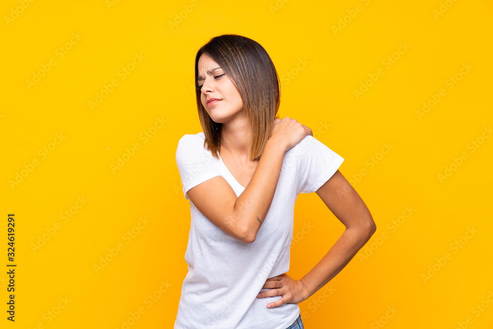 Young woman over isolated yellow background suffering from pain in shoulder for having made an effort Young woman over isolated yellow background suffering from pain in shoulder for having made an effort