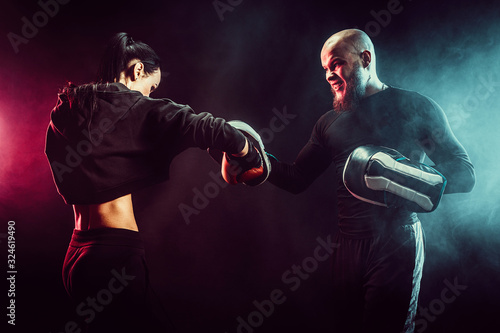 Woman exercising with trainer at boxing and self defense lesson, studio, smoke on background. © zamuruev
