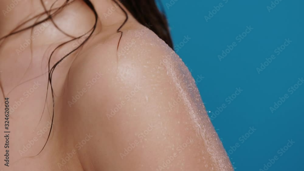 close-up of water drops falling from woman shoulder isolated on blue background close-up of water drops falling from woman shoulder isolated on blue background