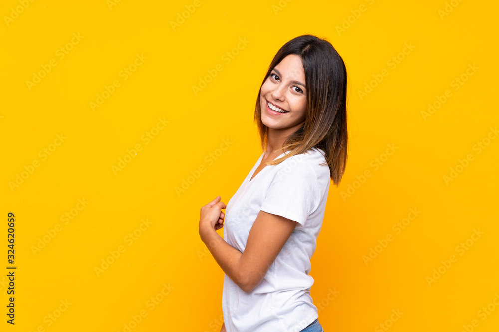 Young woman over isolated yellow background pointing back Young woman over isolated yellow background pointing back
