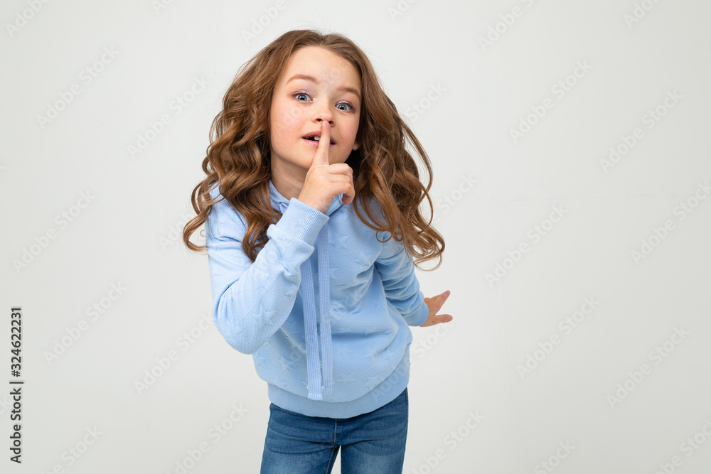 European teenage girl in a blue hoodie asks to be quieter covering her mouth on a white background with copy space European teenage girl in a blue hoodie asks to be quieter covering her mouth on a white background with copy space