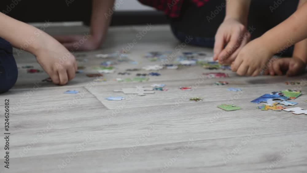 A young mother with two children is sitting on the floor of the room. A happy family puts together a puzzle. Mom helps children. A young mother with two children is sitting on the floor of the room. A happy family puts together a puzzle. Mom helps children.