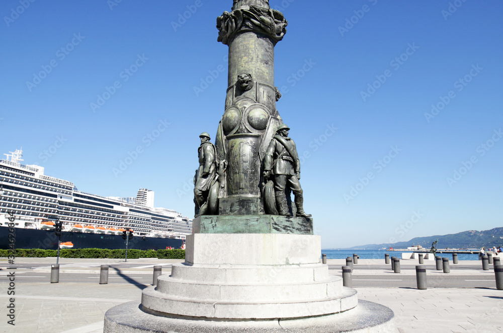 Trieste, Italy.  Popular Cruise Ship Port.  Ornaments at Base of Lamp Post at Piazza Unita di Italia (Unity of Italy Square). Main Focus on Statues in fore ground, cruise ship in background.