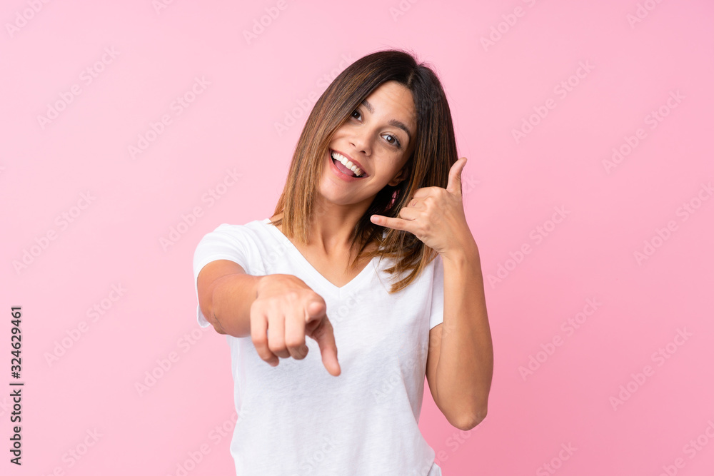 Young woman over isolated pink background making phone gesture and pointing front Young woman over isolated pink background making phone gesture and pointing front