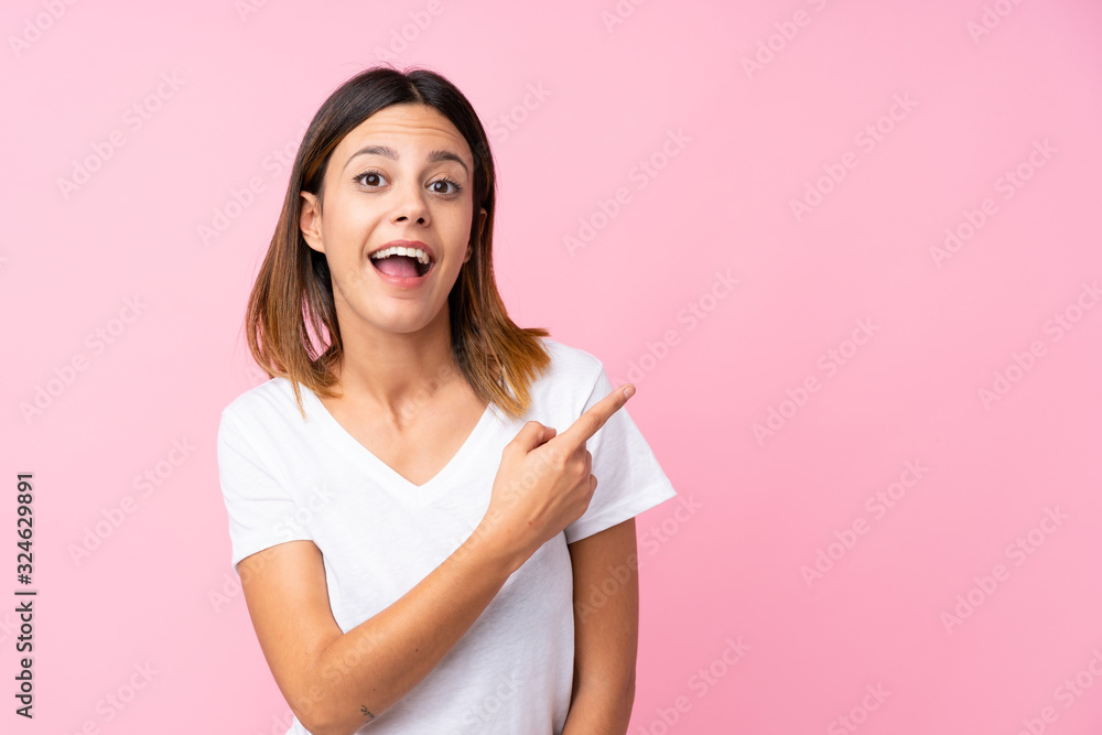 Young woman over isolated pink background surprised and pointing side Young woman over isolated pink background surprised and pointing side