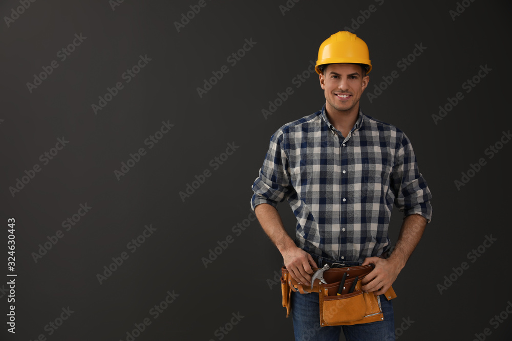 Handsome carpenter with tool belt on dark background. Space for text Handsome carpenter with tool belt on dark background. Space for text