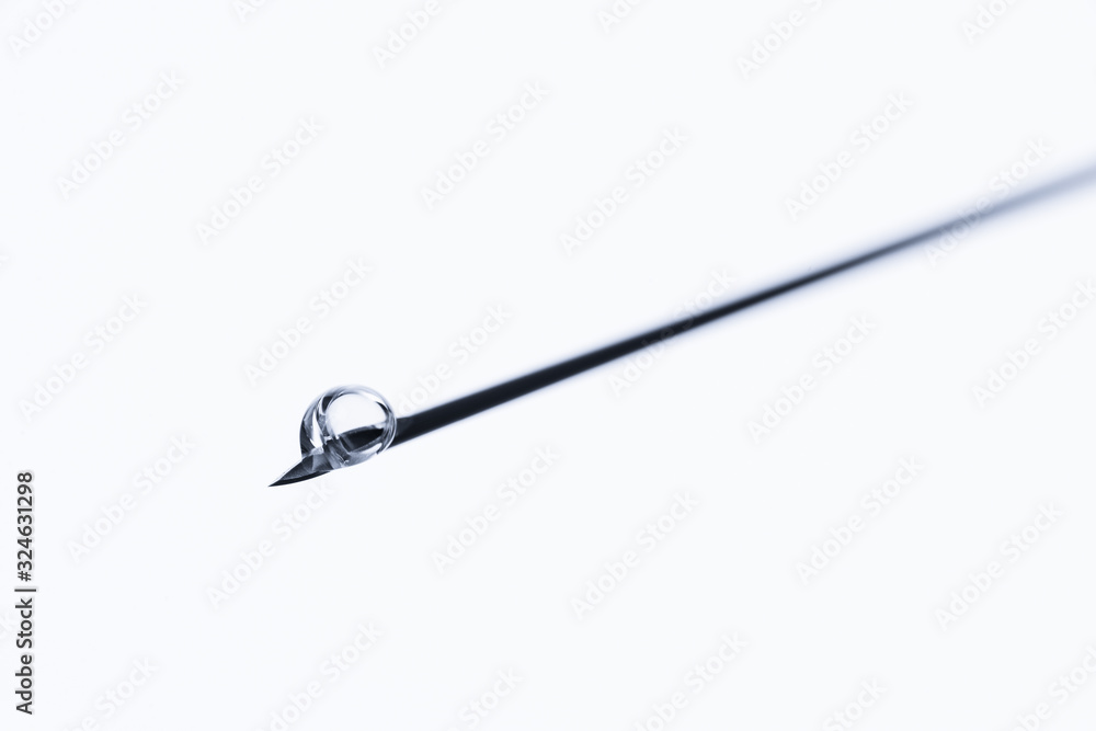 Drop on a medical needle. Macro photo of an injection or vaccination solution on a white background. Drop on a medical needle. Macro photo of an injection or vaccination solution on a white background.