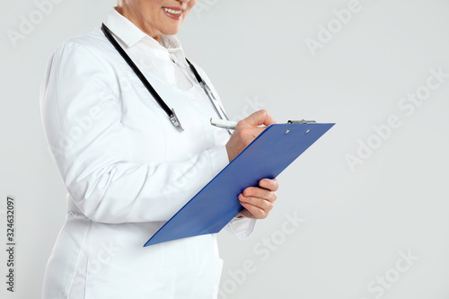 Mature doctor with clipboard on light grey background, closeup © New Africa