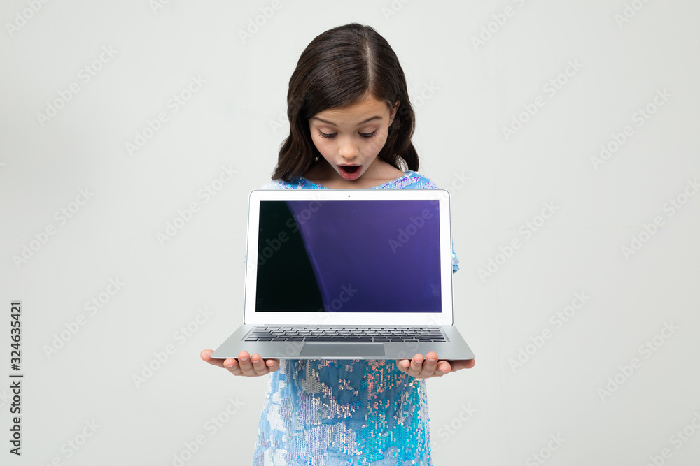 Naklejka premium portrait of a surprised teenager girl holding a laptop with a blank screen to insert a website on a white studio background