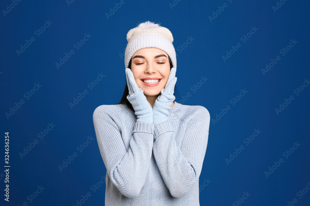 Young woman wearing warm sweater, gloves and hat on blue background. Winter season Young woman wearing warm sweater, gloves and hat on blue background. Winter season