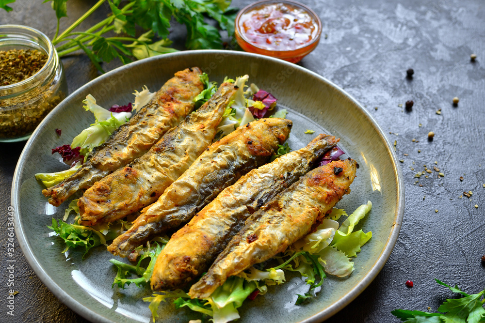 Grilled fish in a gray plate. Small fried fish and salad dressing. Close-up. Grilled fish in a gray plate. Small fried fish and salad dressing. Close-up.