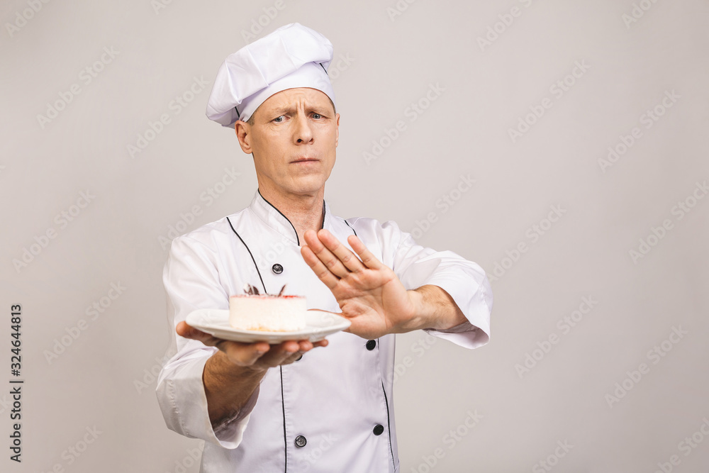 Senior male chef cook or baker man in white uniform posing isolated on white background. Cooking food concept. Showing stop gesture to plate with cake Senior male chef cook or baker man in white uniform posing isolated on white background. Cooking food concept. Showing stop gesture to plate with cake