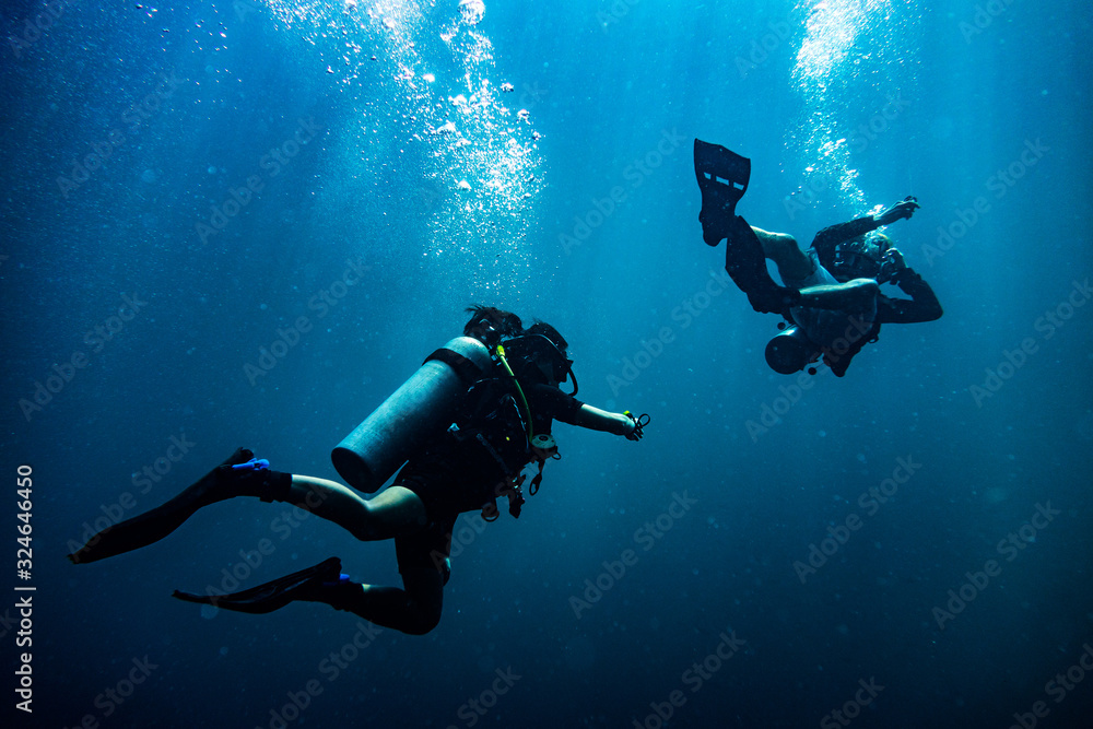 Scuba diver reaching its diving partner in deep blue sea
