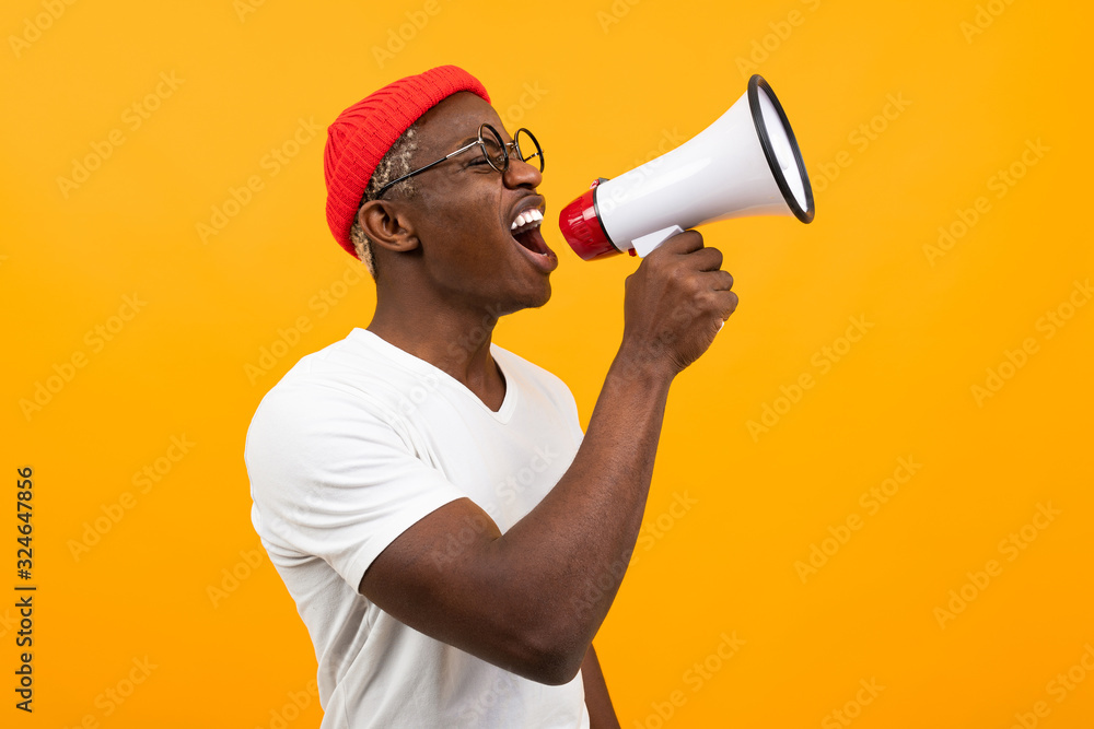 black african man speaks in megaphone on isolated yellow background - obrazy, fototapety, plakaty 