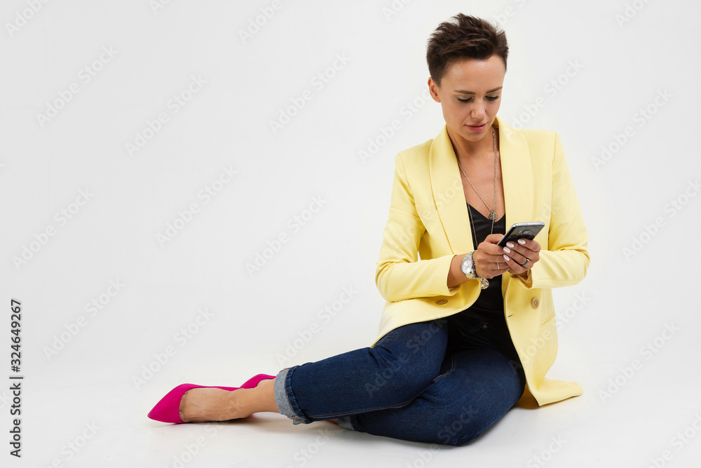 Beautiful young woman in office suit sits on the white floor and serfing internet with her phone Beautiful young woman in office suit sits on the white floor and serfing internet with her phone