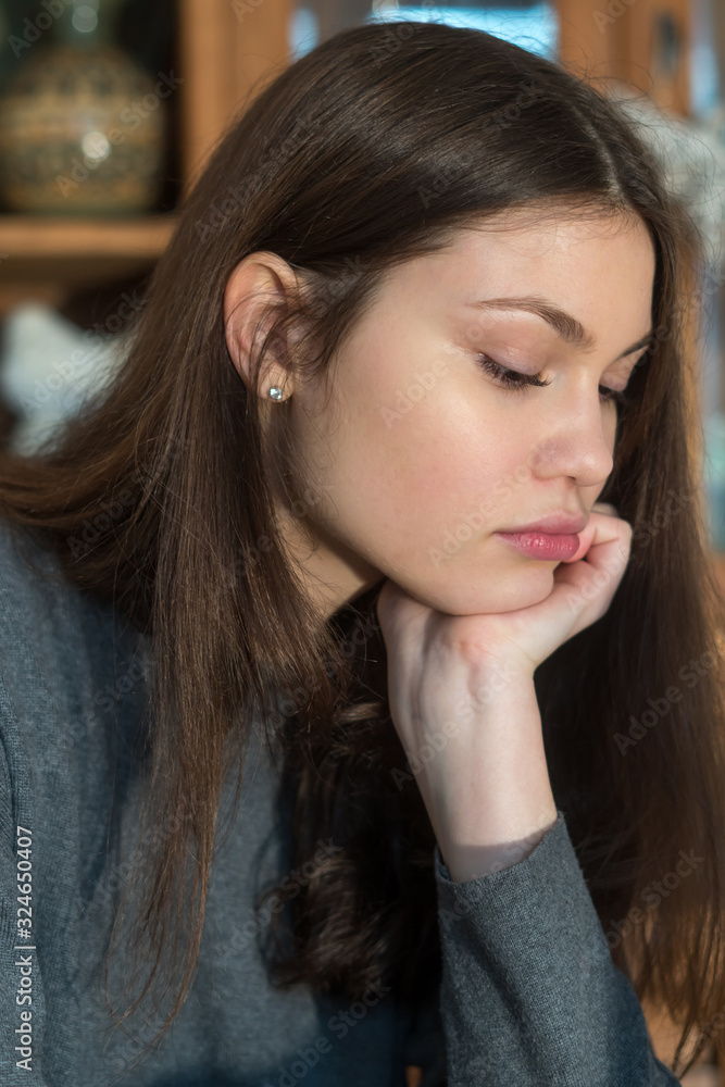Close up portrait of pensive young woman seating at the table while resting her chin on her hand, thinking, looking down. Close up portrait of pensive young woman seating at the table while resting her chin on her hand, thinking, looking down.