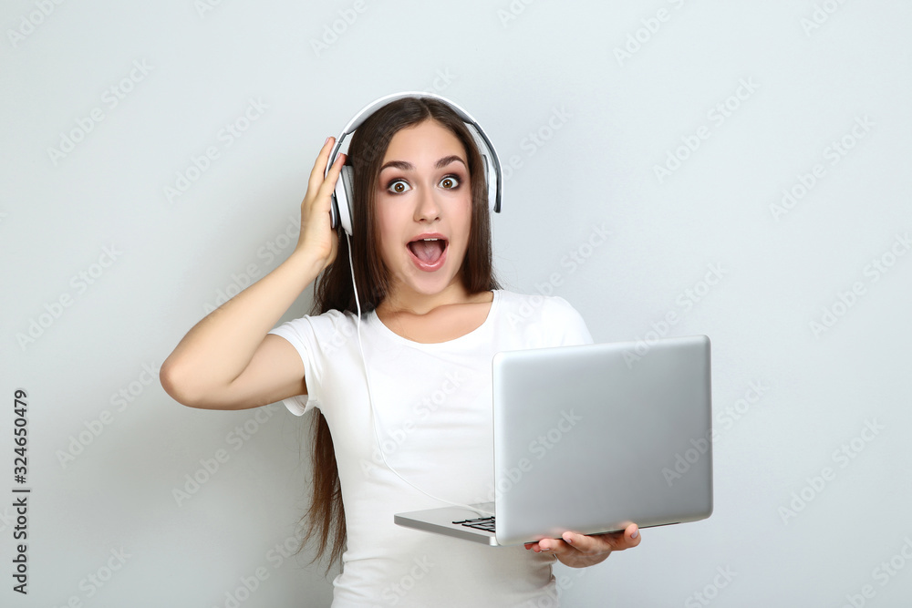 Young girl in headphones with laptop computer on grey background Young girl in headphones with laptop computer on grey background