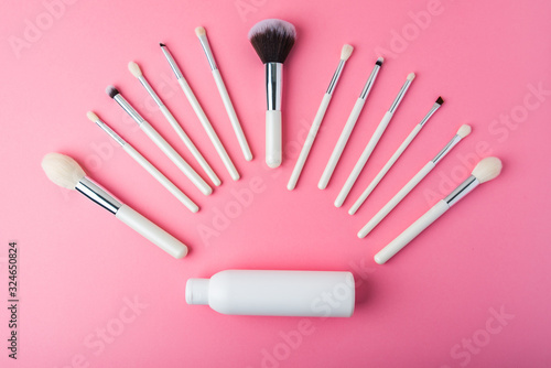 white makeup brushes and tubes on a pink background