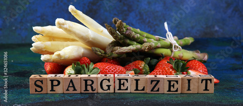 White and green asparagus with strawberries on rustic background with Spargelzeit wooden letter.
