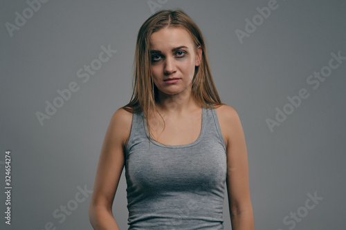 Blonde girl with bruises on her face posing against gray studio background. Domestic violence, abuse. Depression, despair. Close-up, copy space.