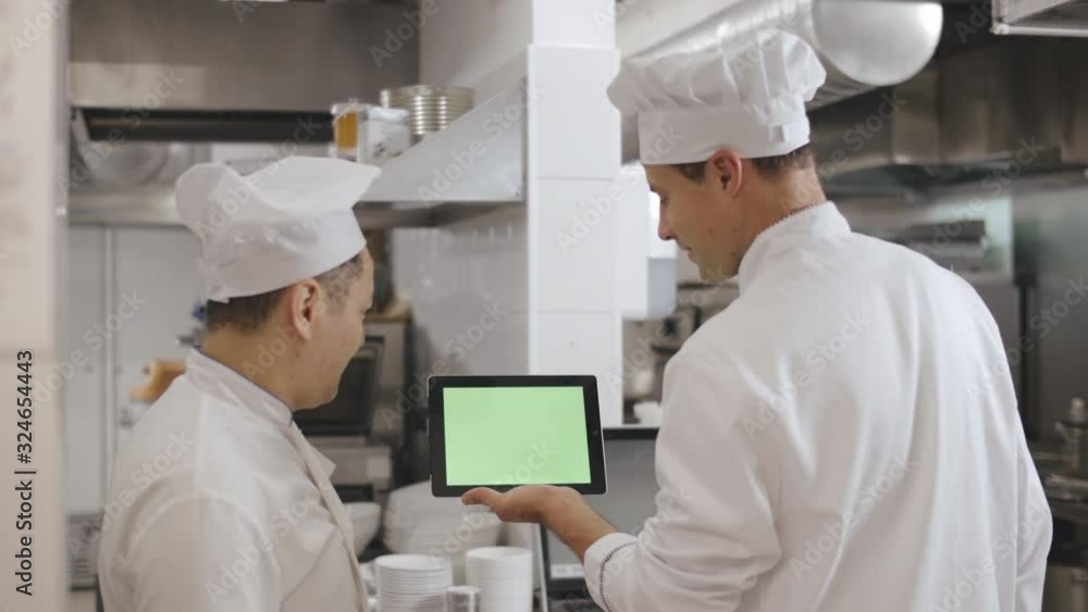 Cooks creating new recipe using digital tablet standing in industrial kitchen Cooks creating new recipe using digital tablet standing in industrial kitchen