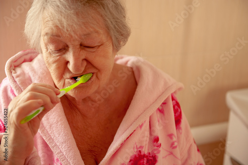 Elderly grandmother in pink terry bathrobe brushes her teeth in bathroom. Hygienic procedures. Pensioners in sanatorium