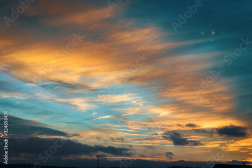 Himmel im Abendlicht mit ziehenden Wolken und Strommast am Horizont in t  rkis und orange