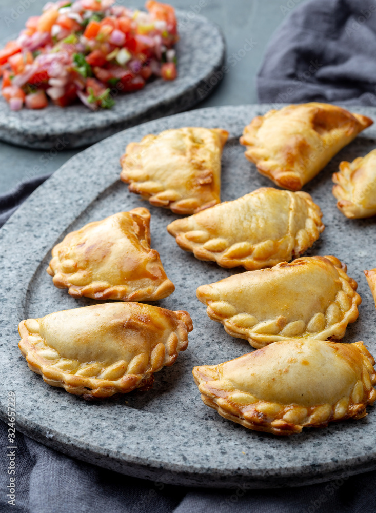 Different little cocktail EMPANADAS on stone plate with tomato sauce and guacamole . Gray background. Latin American and Spanish tipical food Different little cocktail EMPANADAS on stone plate with tomato sauce and guacamole . Gray background. Latin American and Spanish tipical food