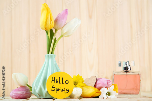 Tulip, chrysanthemum flowers with text Hello Spring and perfume bottle on brown wooden table