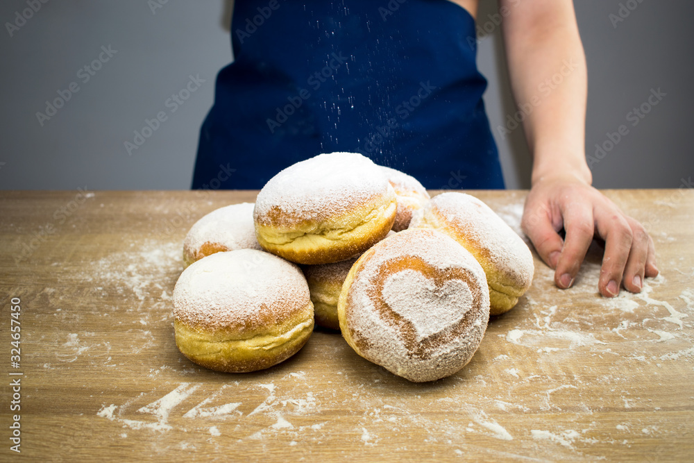 The cook sprinkles icing sugar on fresh donuts. Do-it-yourself donut cooking. The cook sprinkles icing sugar on fresh donuts. Do-it-yourself donut cooking.