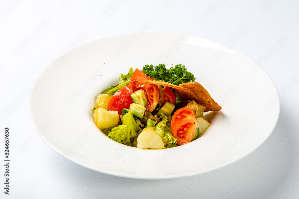 Caesar with chicken and feta cheese.  Served on a round white plate: pieces of fried chicken, cheese, tomatoes, salad. Plate on a white background.