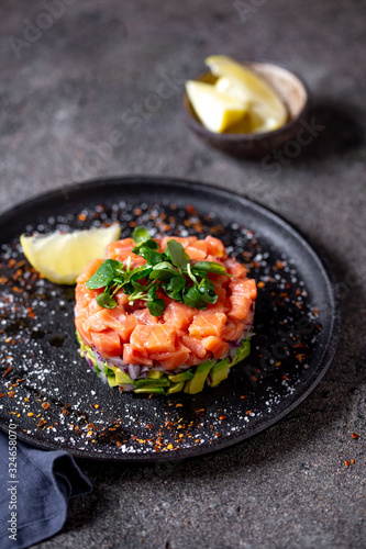 Fototapeta Naklejka Na Ścianę i Meble -  Raw salmon, avocado purple onion salad served in culinary ring on black plate. Black concrete background