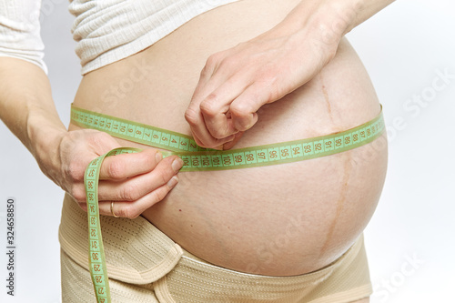 A pregnant woman measures her stomach with a tape measure close-up.