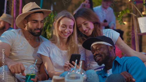 Little group of multi-race cheerful friends taking funny selfie on smartphone spending nice time together on the party. Summer weekend. Friends gathering.