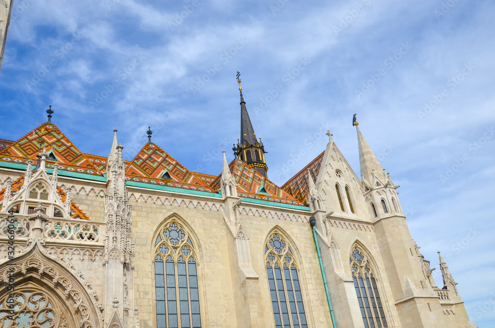 Colored tile roof of the famous Matthias Church in Budapest, Hungary. Roman Catholic church built in the Gothic style. Blue sky and white clouds above. Horizontal photo. Hungarian tourist attraction