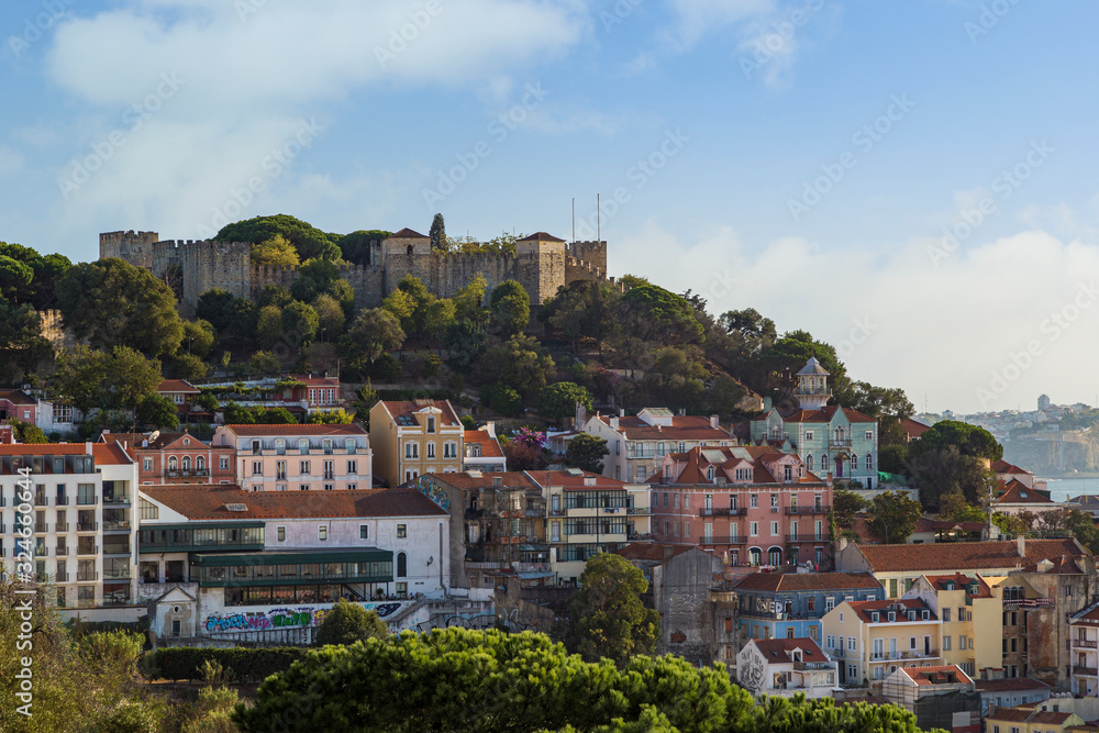 View of the Sao Jorge Castle (Saint George Castle, Castelo de Sao Jorge) and old buildings at the historical Alfama district in downtown Lisbon, Portugal, on a sunny day in the summer. 