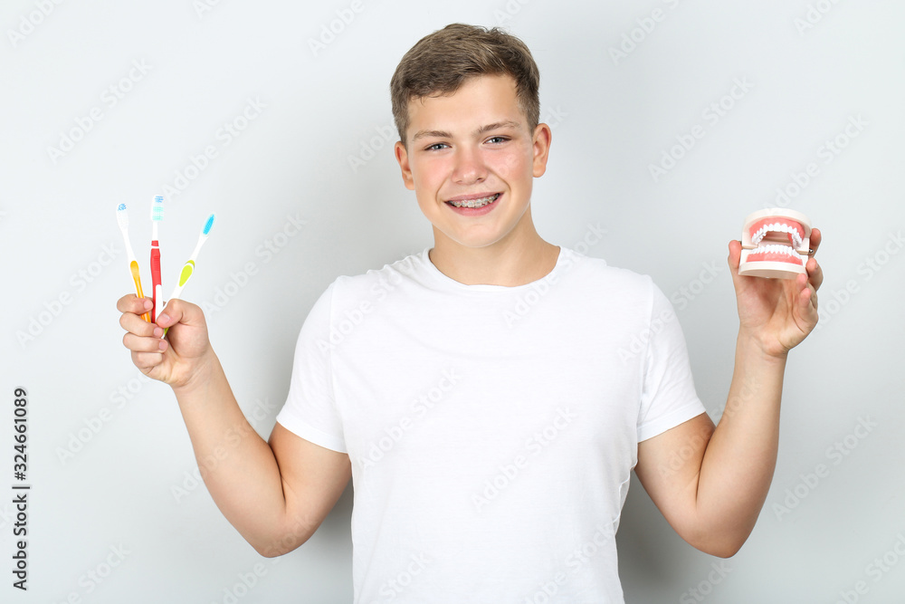 Young man with toothbrushes and teeth model on grey background Young man with toothbrushes and teeth model on grey background